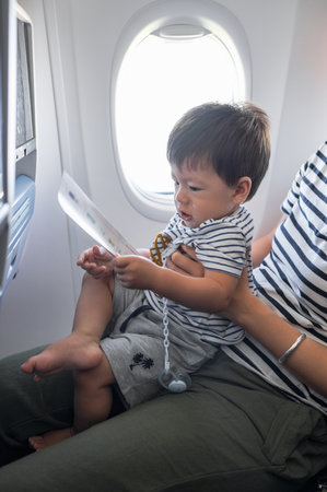 Infant traveling in airplane sitting on its mother lap. One year old baby boy flying in airplane and trying to entertain himselfの写真素材