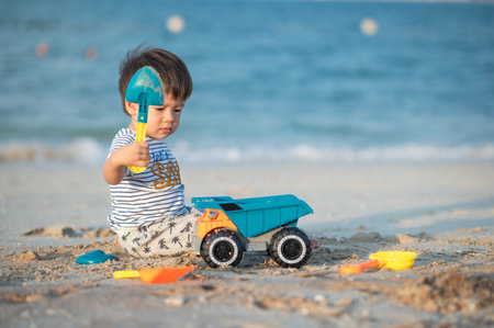 A toddler joyously plays with a toy vehicle on the beach, taking in the wonders of childhood by the sea. Baby boy playing on the beach with a toy truck sitting on the sandの写真素材