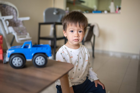 Portrait of one and half year-old baby boy of mixed race sitting on small chair while playing with colorful toy truckの写真素材
