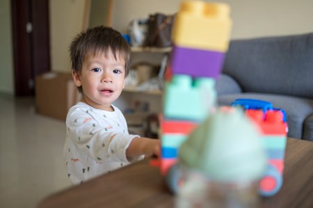 A one and half year-old baby boy of mixed race playing with colorful building blocks and a shape-stacking toy vehicle. Toddler sitting near a coffee table in the living room, enjoying his educational toys at 15 months old.の写真素材