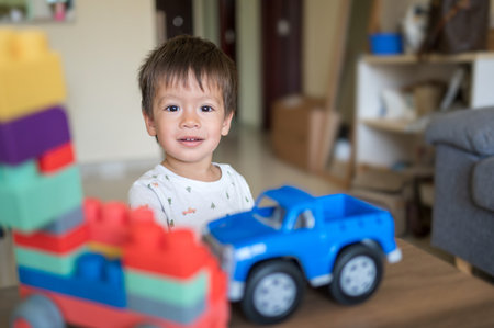 A one and half year-old baby boy of mixed race playing with colorful building blocks and a shape-stacking toy vehicle. Toddler sitting near a coffee table in the living room, enjoying his educational toys at 15 months old.の写真素材