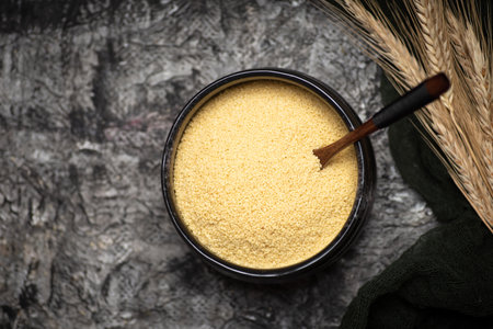 Raw couscous in a black ceramic bowl on a rustic black background table top viewの写真素材