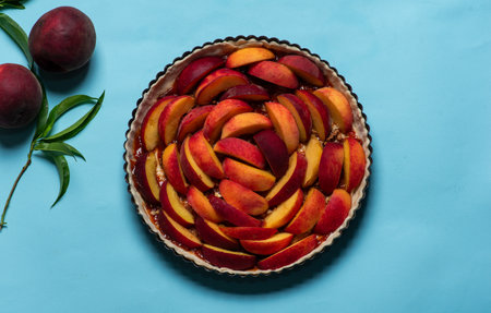 Homemade pie with juicy peaches sprinkled with walnuts. Unbaked, in a baking dish, on a light blue background.の写真素材