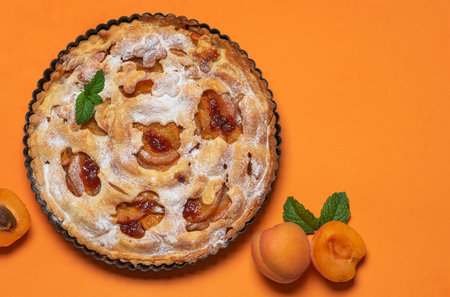 Homemade, freshly baked apricot pie in a baking dish. On an orange background, sprinkled with powdered sugarの写真素材