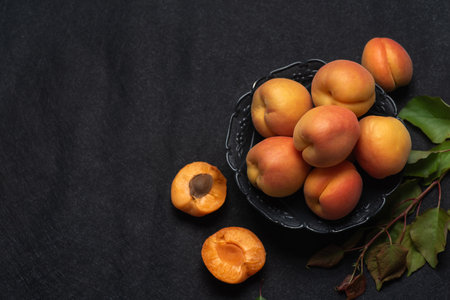 Fresh, ripe, juicy apricots in a black bowl on a black background. Whole fruit, with leaves, apricot halvesの写真素材
