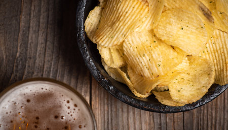 Crispy potato chips in a bowl and light beer in a glass on a wooden backgroundの写真素材