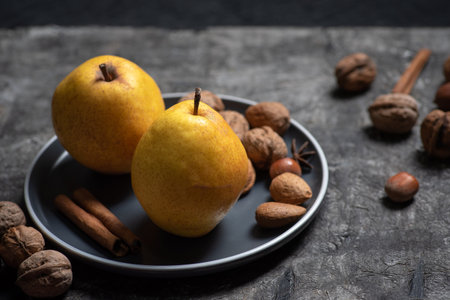 Two fresh, organic yellow pears in a bowl with nuts on a dark wooden backgroundの写真素材
