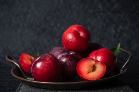 Fresh ripe juicy purple plums in metal bowl on black backgroundの写真素材