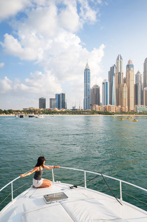 Enchanting beauty of Dubai Marina as a stylish woman embraces the tranquil sunset during a luxurious yacht ride. Capturing the essence of sophistication and relaxation against the iconic cityscape in the United Arab Emiratesの写真素材
