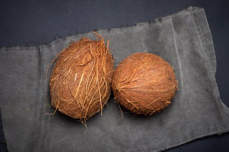 Two whole coconuts on a dark gray background. From above