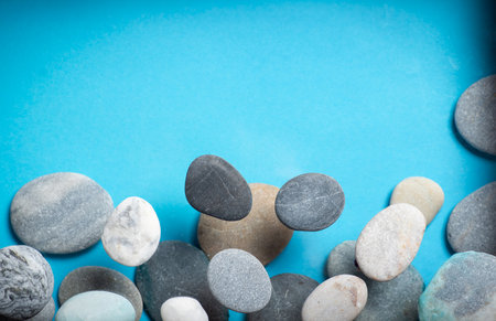 Small stones of different shapes, colors and sizes on a blue background in closeup. With copy space