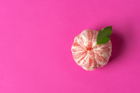 The image showcases a citrus fruit adorned with a leaf, placed against a vivid pink background, emphasizing its freshness and inviting vibrant summer vibes.の写真素材
