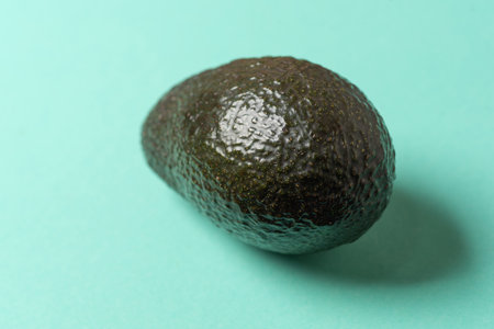 This image features a ripe avocado resting on a bright turquoise background, showcasing its rich...