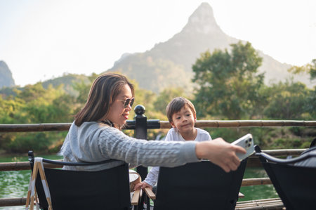 A captivating moment shared between mother and son as they pose for a selfie, framed by the serene river and captivating nature, celebrating the bond of family and adventure.の写真素材