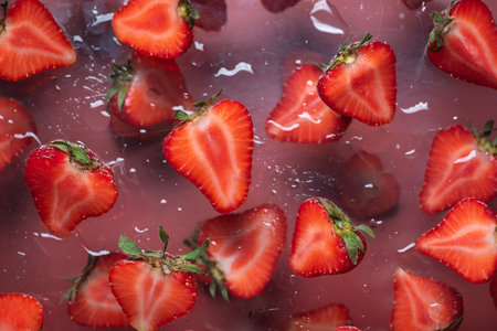 This artistic image features fresh strawberries floating on a clear surface, creatively captured to...