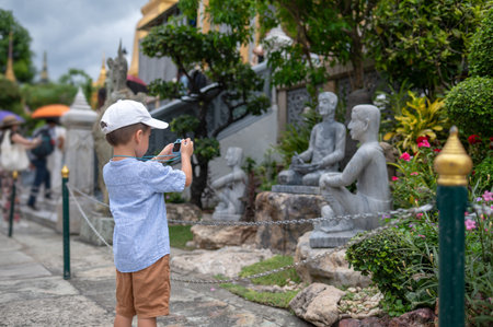The young boy aims his toy camera at picturesque statues amidst lush gardens, embodying the spirit of discovery and creativity while exploring cultural landmarks in a serene environment.の写真素材
