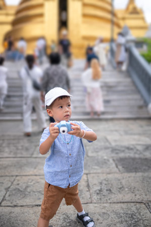 A young boy is joyfully playing with a toy camera while surrounded by people, showcasing a lively atmosphere filled with excitement and adventure in an outdoor location in Bangkok, Thailandの写真素材