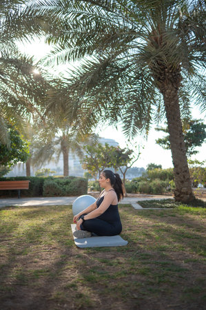 Woman in late pregnancy doing yoga in a park, embodying tranquility and mindfulness, surrounded by...