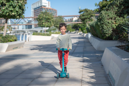 A joyful young boy plays on his kick scooter in Abu Dhabi's Al Raha, showcasing the excitement of...