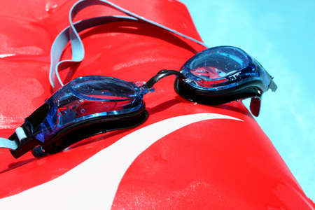 Blue swimming goggles on red boogie board, floating in swimming pool