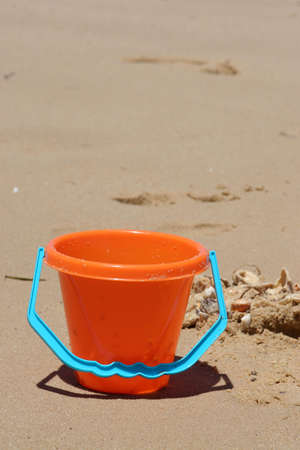 Orange plastic bucket on beach with shellsの写真素材