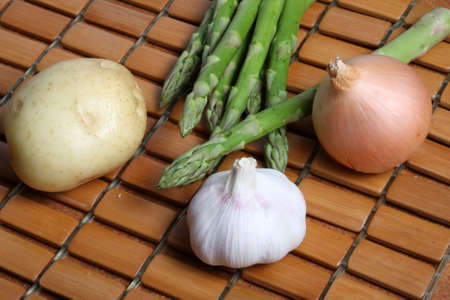 Close up of asparagus spears potato brown onion and garlic cloves on wooden tile kitchen matの写真素材