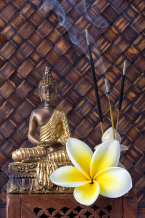 buddha idol with incense sticks and frangiapani flower against bamboo backgroundの写真素材