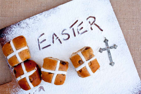 hot cross buns on floured wooden cutting board, with word Easter written in flour - with silver crossの写真素材