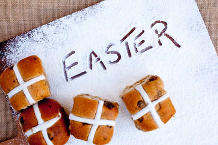 hot cross buns on floured wooden cutting board, with word Easter written in flourの写真素材
