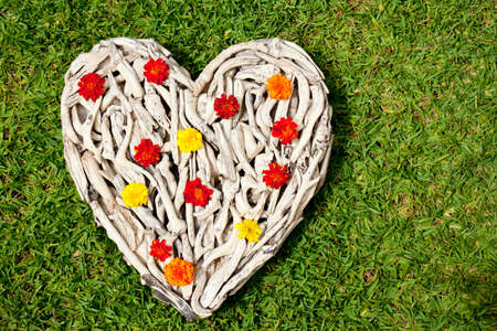 Driftwood Heart on grass background - with orange and yellow flowersの写真素材