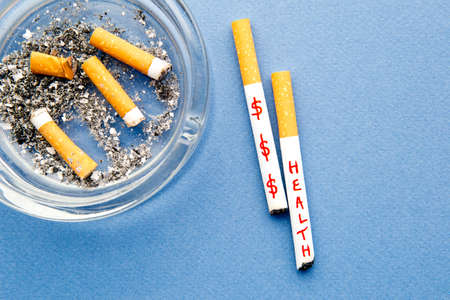 Stop Smoking - Health and Money - with cigarettes and ashtray on blue background