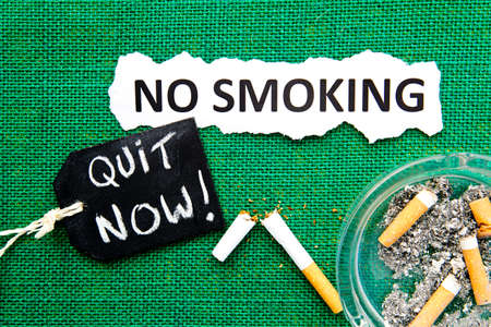 No Smoking - with ashtray, broken cigarette, handwritten blackboard and printed text on green burlap backgroundの写真素材