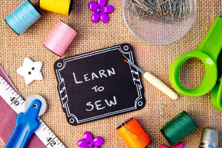 Sewing - Learn to Sew on blackboard with cotton reels, pins, tape measure on burlap backgroundの写真素材