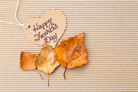 Happy Father's Day - on heart shape tag on corrugated cardboard background with autumn leavesの写真素材