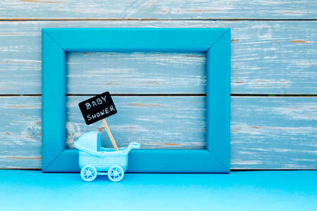 Baby Shower - toy pram with backboard sign with blue frame and wooden backgroundの写真素材