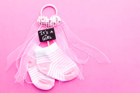 Baby Girl announcement - pink and white socks with heart on pink background with It's a Girl blackboard signの写真素材