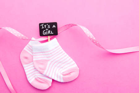Baby Girl - pink and white socks with ribbon on pink background with It's a Girl blackboard signの写真素材
