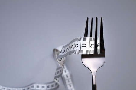 Measuring tape and fork on the grey background. The concept of healthy food and diet. Copy space.の写真素材