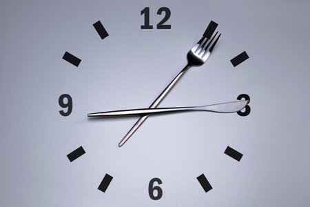 Clock with cutlery, grey background. The concept of intermittent fasting, lunchtime, diet and weight loss.の写真素材