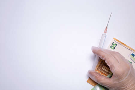 Hand holds syringe with vaccine, cash on the background. Free space for text.の写真素材