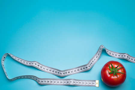 Tomato and measuring tape on the blue background. The concept of diet. Free space for text.