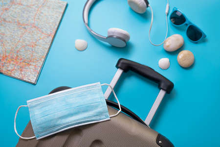 Medical mask, suitcase, sun glasses, map, seashells on the blue background.の写真素材