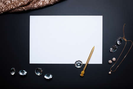 White, empty paper sheet, jewelry and other accessories on the black background. Free space, copy space. Fashion, beauty backdrop. Top view, modern flat lay.の写真素材