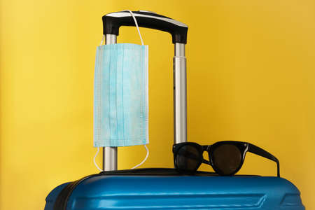 Travel during the time of COVID-19. Medical mask, suitcase, sun glasses on the yellow background. Vacation, holidays in corona times.の写真素材