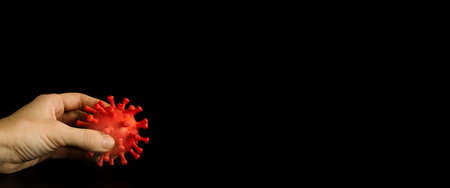 Little, red coronavirus model in the hand on the black background. Covid 19 virus, pandemic. Corona...