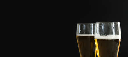 Two frosty glasses of cold golden beer with bubbles on the black background. Free space for text, copy space, banner. Drinking alcohol on party, holidays, Oktoberfest or St. Patricks Day.の写真素材