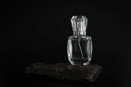 Unbranded perfume bottle standing on stone podium. Perfume presentation on the black background. Mockup. Trending concept in natural materials. Womens and mens essence. Natural cosmetic.の写真素材