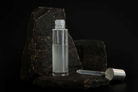 Unbranded natural cosmetic serum packaging standing on stone podium. Serum presentation on the black...