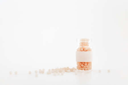 Close-up image of homeopathic globules in glass bottle on white background. Homeopathy pharmacy, herbal, natural medicine, alternative homeopathy medicine, healthcare. Free space, copy space.の写真素材