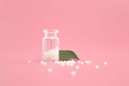 Close-up image of homeopathic globules in glass bottle on pastel pink background. Homeopathy pharmacy, herbal, natural medicine, alternative homeopathy medicine, healthcare. Free space, copy space.の写真素材